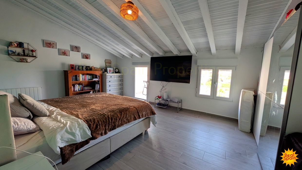 Large bedroom at Cortijo Salud with bed, television and light painted beams